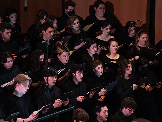 An array of choral singers, donning black attire, in warm lighting.