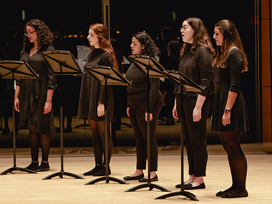 A group of choral singers wearing black and standing on stage.