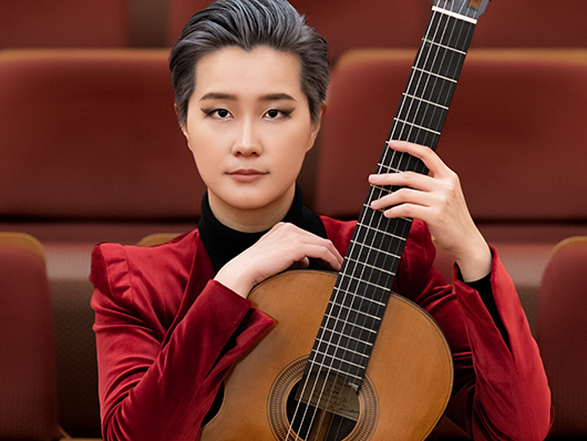 A portrait of Meng Su with her guitar in an empty theater