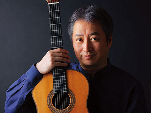 A portrait of Shin-ichi Fukuda in navy blue, holding his guitar