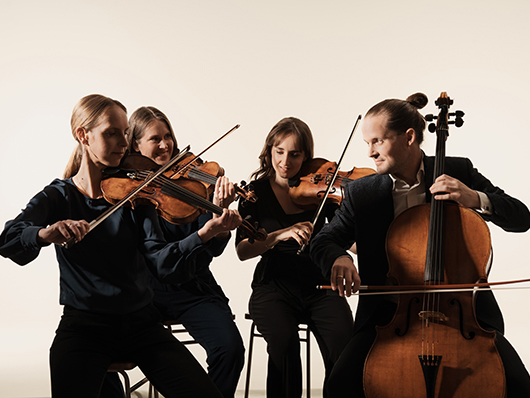 The members of the Dudok Quartet Amsterdam sit playing their instruments against a white backdrop