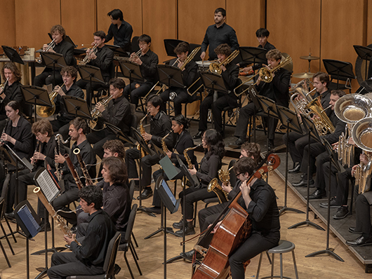 A large band plays onstage, playing woodwinds, brass, and strings.