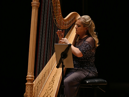 Marguerite Lynn Williams sits onstage playing the harp.