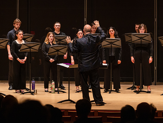 A conductor stands with his hands up, conducting a choir of students.