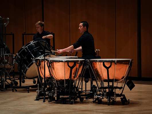 A drummer plays four timpanis while another plays a bass drum.