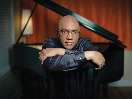 Billy Childs leans over an open piano.