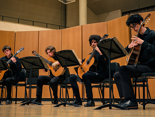 Four classical guitarists play seated.