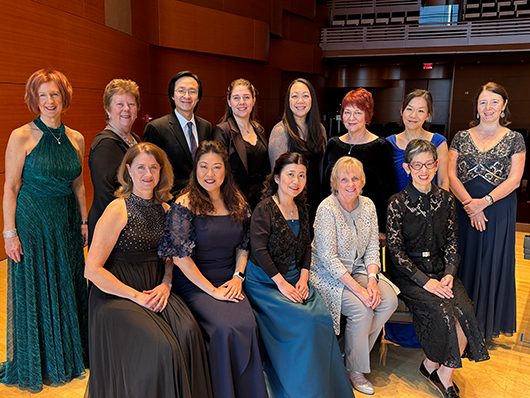 The music academy faculty stands and sits, smiling for the camera in the concert hall.