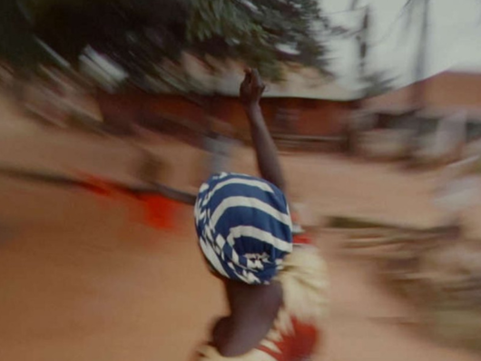 A woman with striped head wrap and raised arm in a blurry landscape