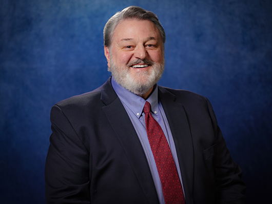 Stanford Olsen standing against a blue background, wearing a suit and tie