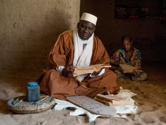 man sitting cross-legged with child sitting cross-legged behind him