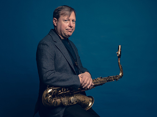 Chris Potter holding saxophone, standing against teal background