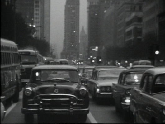 black and white film still of cars driving through downtown chicago