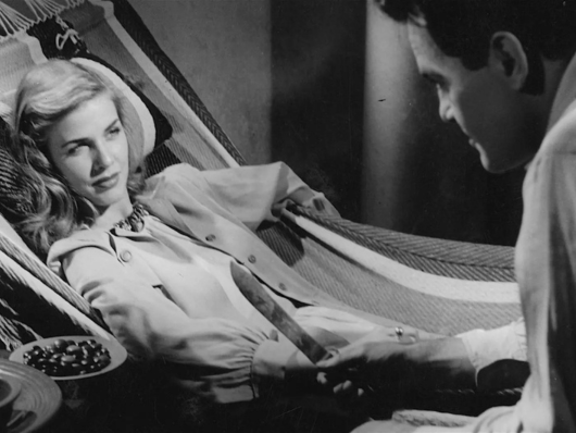Black and white film still of reclining woman glaring at man