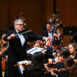 Conductor Victor Yampolsky in front of Northwestern University Symphony Orchestra performing on a well lit stage