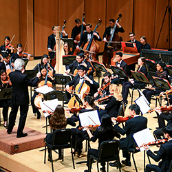 Conductor in front of Northwestern University Chamber Orchestra performing on well lit stage