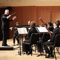 Daniel J. Farris in front of Concert Band performing on well lit stage