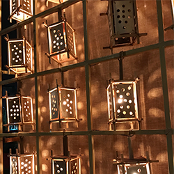 A low-light photograph of a grid of wooden lanterns with circles on each side letting out light.
