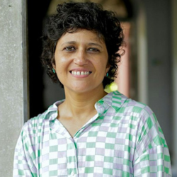 A headshot of Priya Sen smiling, wearing a checkered shirt