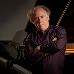 A portrait of Jeffrey Kahane posing next to a piano