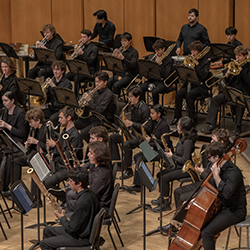 A large band plays onstage, playing woodwinds, brass, and strings.