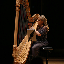 Marguerite Lynn Williams sits onstage playing the harp.