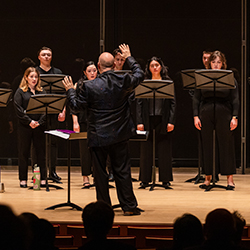 A conductor stands with his hands up, conducting a choir of students.