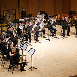 A semicircle of brass players perform as a conductor leads from the front.