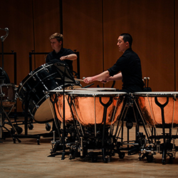 A drummer plays four timpanis while another plays a bass drum.