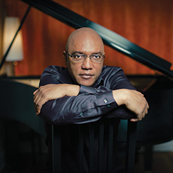 Billy Childs leans over an open piano.