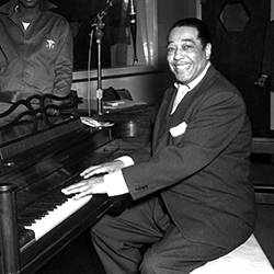 Duke Ellington sits at a piano, grinning broadly.