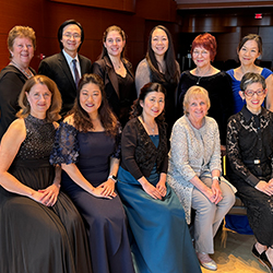 The music academy faculty stands and sits, smiling for the camera in the concert hall.