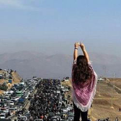 Girl on a cliff holding up her arms facing a protest