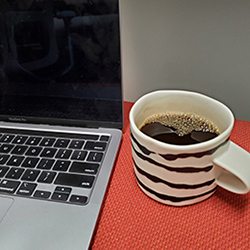 corner of an open laptop with a full cup of coffee next to it