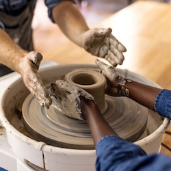 Hands making pottery on a wheel guided by a teacher