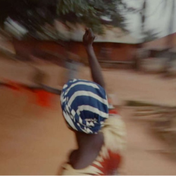 A woman with striped head wrap and raised arm in a blurry landscape