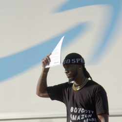 A man wearing a black "Boycott Amazon" shirt and cap shields his eyes from the sun