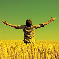 A young man stands in a field with his arms extended out to his sides