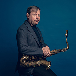 Chris Potter holding saxophone, standing against teal background