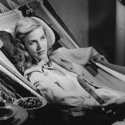 Black and white film still of reclining woman glaring at man